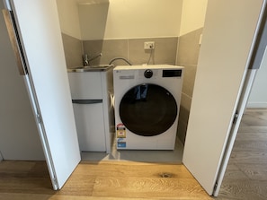 A compact laundry area with a washing machine and a small sink. - Stylish 2BDR Collingwood Apartment with Parking (Collingwood)