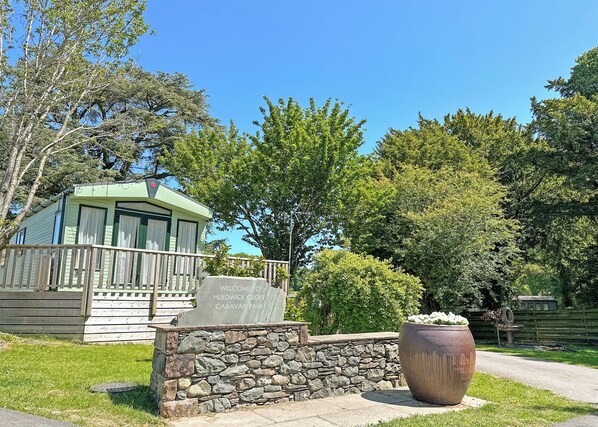 A caravan park entrance with a stone wall, a wooden sign, and a large planter. - Superior Hot Tub 2 bed Holiday Home sleeps 4 Pet (Bassenthwaite, near Keswick)