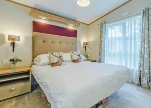 Ein Hotelzimmer mit einem großen Bett, zwei Nachttischen, einem Kopfteil und einem Fenster mit Vorhängen.