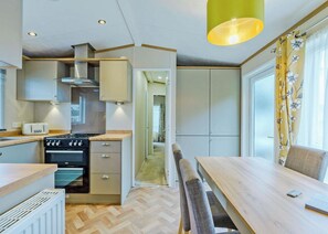 A modern kitchen with a dining area, wooden flooring, and a view through the open door. - Superior Hot Tub 2 bed Holiday Home sleeps 4 Pet (Bassenthwaite, near Keswick)