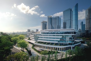 A modern hotel with a curved facade, surrounded by lush greenery and high-rise buildings. - Hotel Indigo Suzhou Jinji Lake (Suzhou)