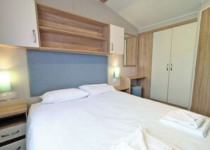 Habitación de hotel con cama, cabecera de madera, mesitas de noche, un armario y una mesita auxiliar.