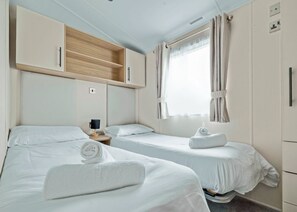 A hotel room with two beds, a wooden cabinet, a nightstand with a lamp, and a window with curtains. - Tweed Spa + - 2 Bedroom (Pet Friendly) (Coldstream)