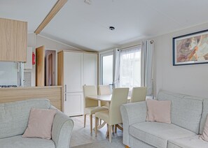 A modern living room with a sofa, a dining table with chairs, and a kitchen area with cabinets and a refrigerator. - Tweed Spa + - 2 Bedroom (Coldstream)