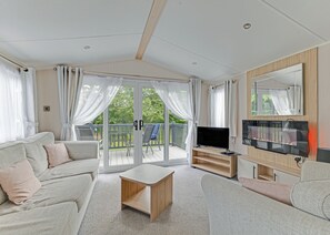 A spacious living room with a sofa, a coffee table, a TV, and a balcony with curtains. - Tweed Spa + - 2 Bedroom (Coldstream)