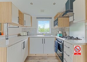A compact kitchen with white cabinets, a stainless steel range hood, a built-in microwave, and a gas stove. - Tweed Spa + - 2 Bedroom (Coldstream)