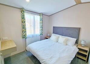 A bedroom with a bed, a nightstand, a lamp, a window with curtains, and a radiator. - Tweed Spa + - 3 Bedroom (Pet Friendly) (Coldstream)