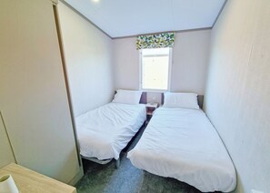 A small, compact room with two single beds, a window with a colorful curtain, and a small table. - Tweed Spa + - 3 Bedroom (Pet Friendly) (Coldstream)