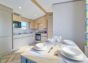 A modern kitchen with wooden cabinets, a microwave, a stove, and a dining area set with plates, glasses, and cutlery. - Tweed Spa + - 3 Bedroom (Pet Friendly) (Coldstream)