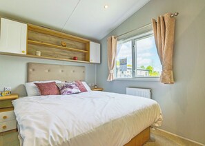Ein Schlafzimmer mit einem Bett, einem Nachttisch, einer Kommode, einem Fenster mit Vorhängen und einer Heizung.