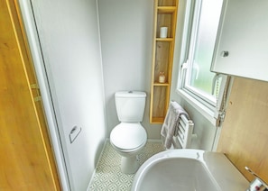 Ein kleines Badezimmer mit Toilette, Waschbecken und einem Holzregal mit Toilettenartikeln.