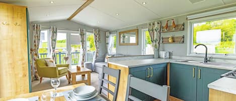 A modern kitchen with a dining area, wooden flooring, and a view of greenery outside.