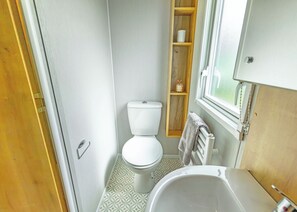 Ein kleines Badezimmer mit Toilette, Waschbecken und einem Holzregal mit Toilettenartikeln.