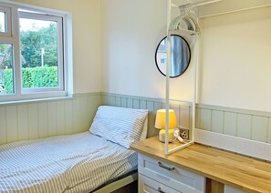 Yhden hengen sänky, jossa on raidallinen päiväpeite, yöpöytä lampun kanssa, peili ja ikkuna, josta avautuu näkymä vehreään maisemaan.