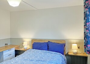 Een slaapkamer met een bed, twee nachtkastjes, een lamp en een stopcontact.