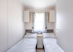 A compact bedroom with two single beds, a small window with curtains, and a wooden headboard. - Spa Luxe - 2 Bedroom (Coldstream)