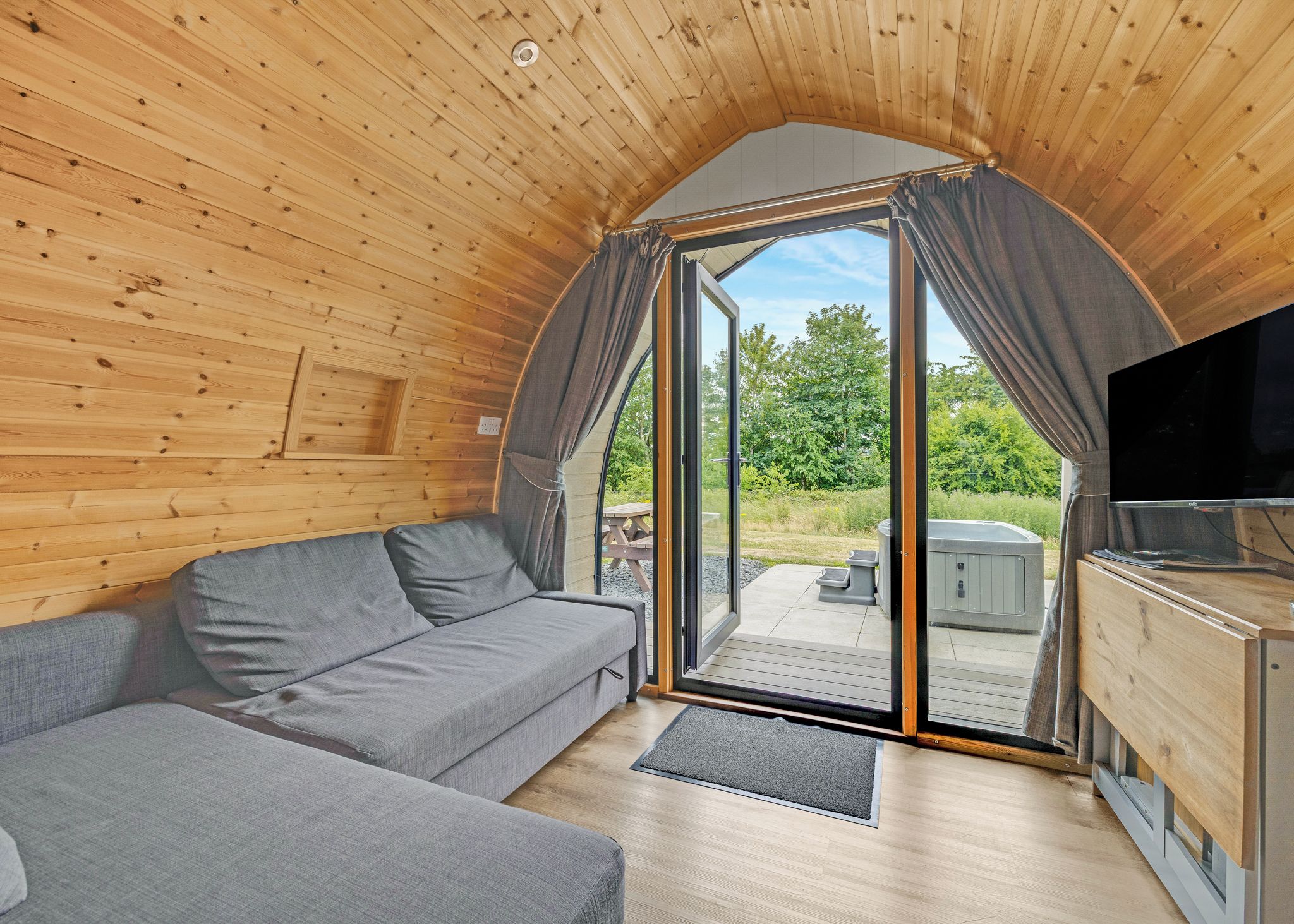 Un intérieur de chalet chaleureux avec un canapé, un téléviseur et une porte-fenêtre coulissante donnant sur un espace extérieur.