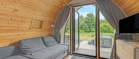 A cozy cabin interior with a sofa, a television, and a sliding glass door leading to an outdoor area.
