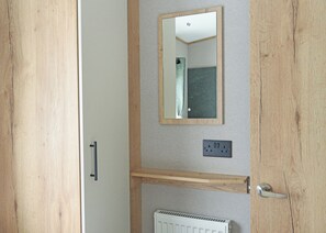 Ein Zimmer mit Holztür, Spiegel, Heizkörper und einer Steckdose an der Wand.