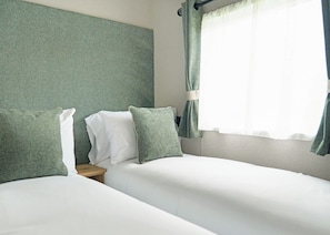 Ein Hotelzimmer mit Bett, Kissen, einem Nachttisch und einem Fenster mit Vorhängen.