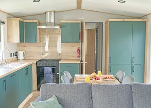 A compact kitchen with a stove, sink, and a dining area with a table set for breakfast. - Luxury 3 Bedroom Holiday Home (Bassenthwaite, near Keswick)