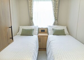 A twin bedroom with two beds, a nightstand, and a window with curtains. - Luxury 3 Bedroom Holiday Home (Bassenthwaite, near Keswick)