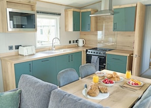 A compact kitchen with a gas stove, sink, and a dining area with breakfast items. - Luxury 3 Bedroom Holiday Home (Bassenthwaite, near Keswick)