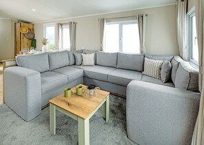 Un salon moderne avec un canapé d’angle gris, une table basse en bois et un coin repas comprenant une table et des chaises en bois.