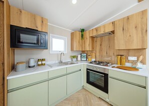 A modern kitchen with wooden cabinets, a built-in microwave, a gas stove, and a window. - Luxury 2 Bedroom Holiday Home – Pet Friendly (Bassenthwaite, near Keswick)
