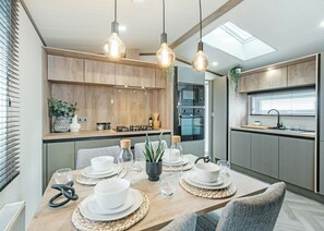 A modern kitchen with wooden cabinets, a dining area with a table set for four, and pendant lighting. - Premium 2 Bedroom Holiday Home - Pet Friendly (Bassenthwaite, near Keswick)