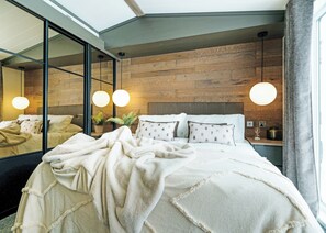 A modern bedroom with a large bed, a wooden headboard, and a large mirror. - Premium 2 Bedroom Holiday Home - Pet Friendly (Bassenthwaite, near Keswick)