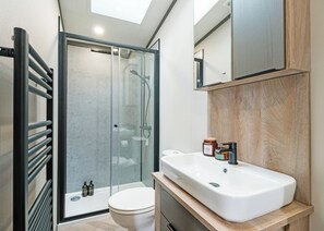 Ein modernes Badezimmer mit Duschkabine aus Glas, einem weißen Waschbecken und einem Holzlagerfläschchen.