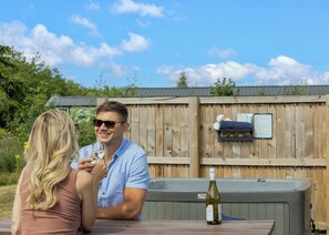 Ett trästaket med en skylt, en vinflaska och ett bord med två personer.