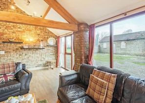 A cozy living room with leather sofas, a brick wall, and large windows. - 1 bedroom accommodation in Beverley (Beverley)