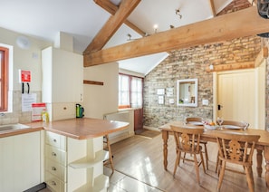 A kitchen with wooden beams, a stone wall, and a dining area with a table and chairs. - 1 bedroom accommodation in Beverley (Beverley)