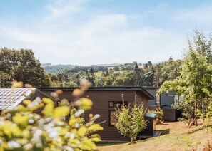 A modern cabin with a sloped roof, surrounded by a forested landscape and a view of rolling hills in the distance. - Cherry Lodge VIP Hot Tub and Pet Friendly (Bridgnorth)