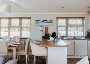 Une cuisine moderne dotée d’un îlot central, d’un coin repas avec des chaises et offrant une vue dégagée grâce à de grandes fenêtres.
