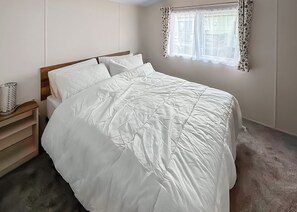 A bedroom with a bed, a nightstand, a window with patterned curtains, and a plain wall. - 2 bedroom accommodation in Stamford Bridge, York (Stamford Bridge, York)