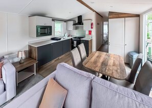 A compact kitchen with modern appliances, a dining area with a wooden table and chairs, and a living space with a sofa and a lamp. - 2 bedroom accommodation in Stamford Bridge, York (Stamford Bridge, York)