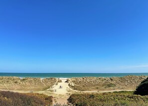 A coastal landscape with a sandy beach, grassy dunes, and a clear blue sky. - 0 bedroom accommodation in Hemsby (Hemsby)