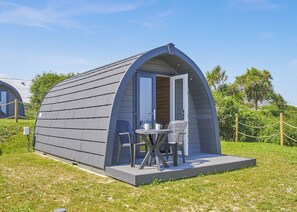 A small, single-room structure with a curved roof, a door, and a small patio area with a table and chairs. - 0 bedroom accommodation in Hemsby (Hemsby)