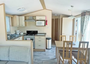 A compact kitchen with a stove, microwave, and cabinets. There is a dining area with a table and chairs. - 2 bedroom accommodation in Cannock Chase (Cannock Chase)
