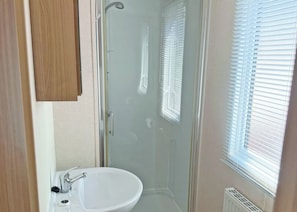 A bathroom with a glass shower enclosure, a sink, and a window with blinds. - 2 bedroom accommodation in Cannock Chase (Cannock Chase)