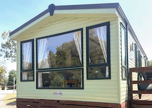 A mobile home with a large bay window, a wooden deck, and a visible logo on the front. - 2 bedroom accommodation in Cannock Chase (Cannock Chase)