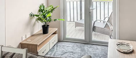 A compact living space with a sofa, a small table, a potted plant, and a sliding glass door leading to an outdoor deck.