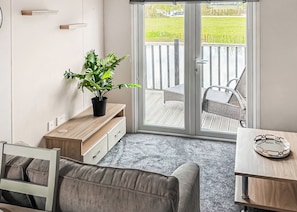 A compact living space with a sofa, a small table, a potted plant, and a sliding glass door leading to an outdoor deck. - 2 bedroom accommodation in Bubwith (Bubwith)