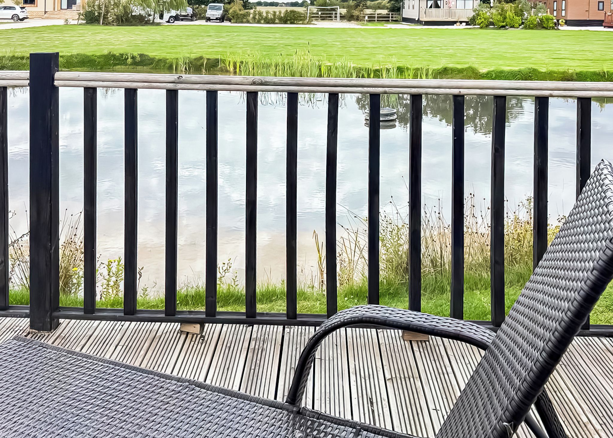 A wooden deck with a metal railing overlooking a grassy area and a body of water.