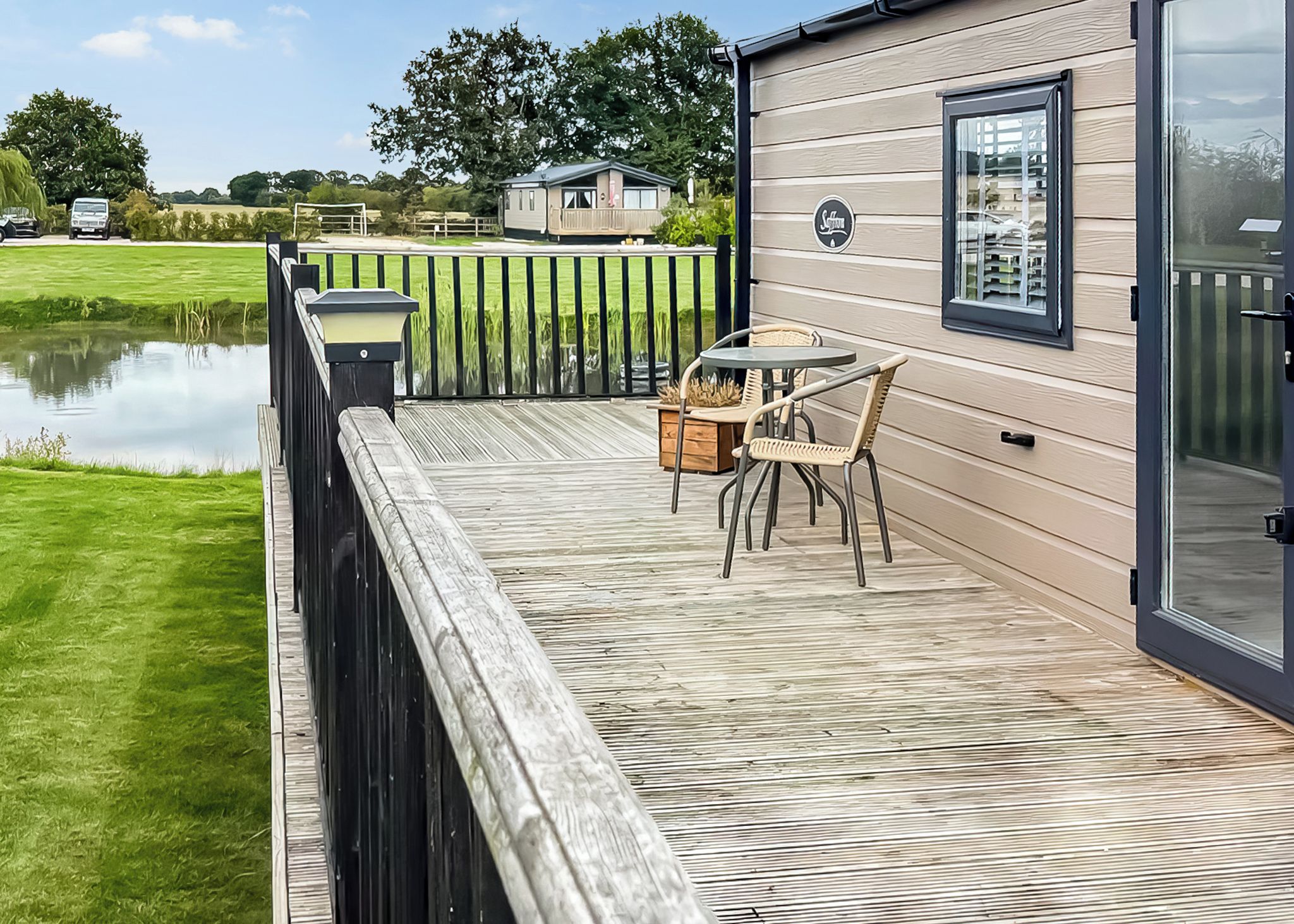 Une terrasse avec une table et des chaises, une clôture en bois et une étendue d’eau en arrière-plan.