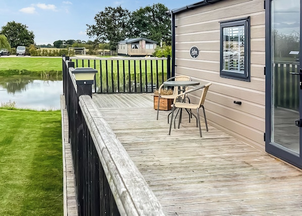 A deck with a table and chairs, a wooden fence, and a body of water in the background. - 2 bedroom accommodation in Bubwith (Bubwith)