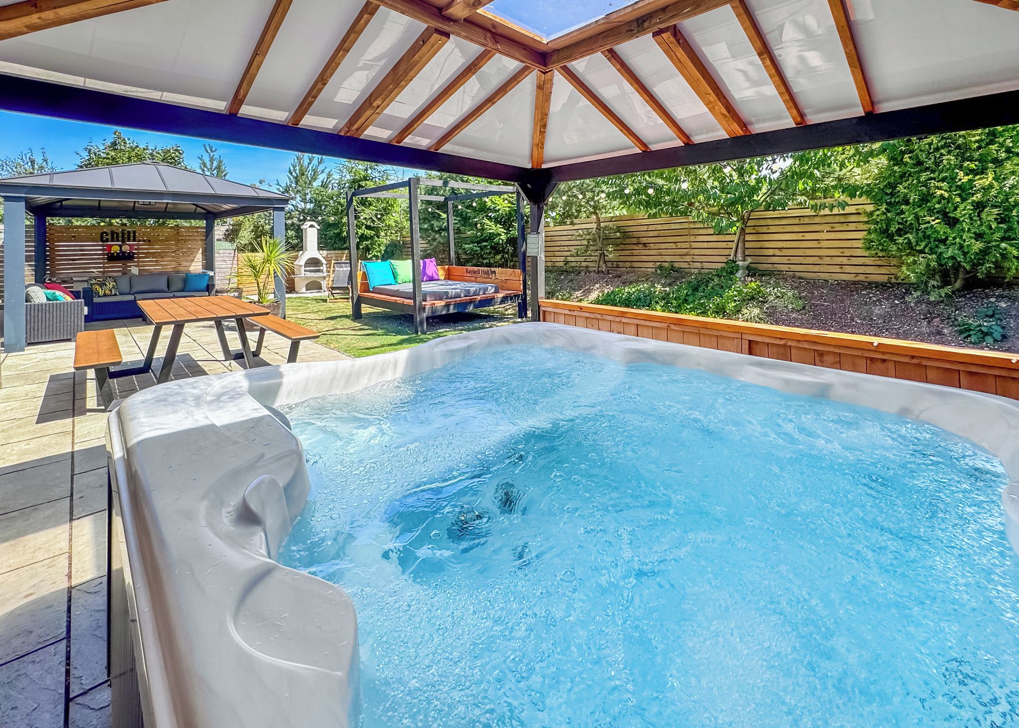 Ein Whirlpool unter einer Holzpergola mit einer Terrasse, Sitzgelegenheiten im Freien und einem Grill.